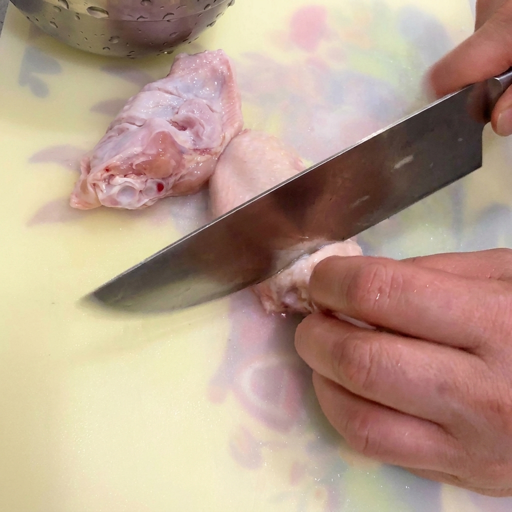 Ali di pollo, zenzero e cipollotto in una pentola di acqua fredda pronti per essere sbollentati.