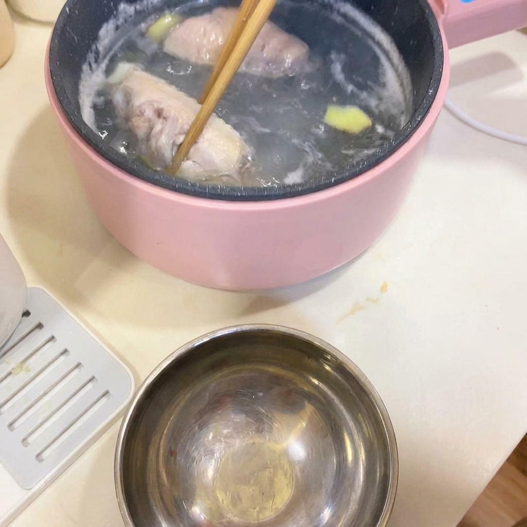 Bacchette che sollevano le ali di pollo sbollentate dalla pentola di cottura.