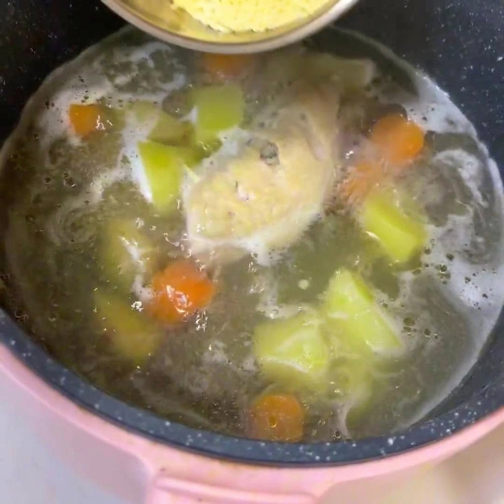 Una pentola di brodo bollente con pollo, patate a cubetti e carote, in cui viene mescolata la pastina.