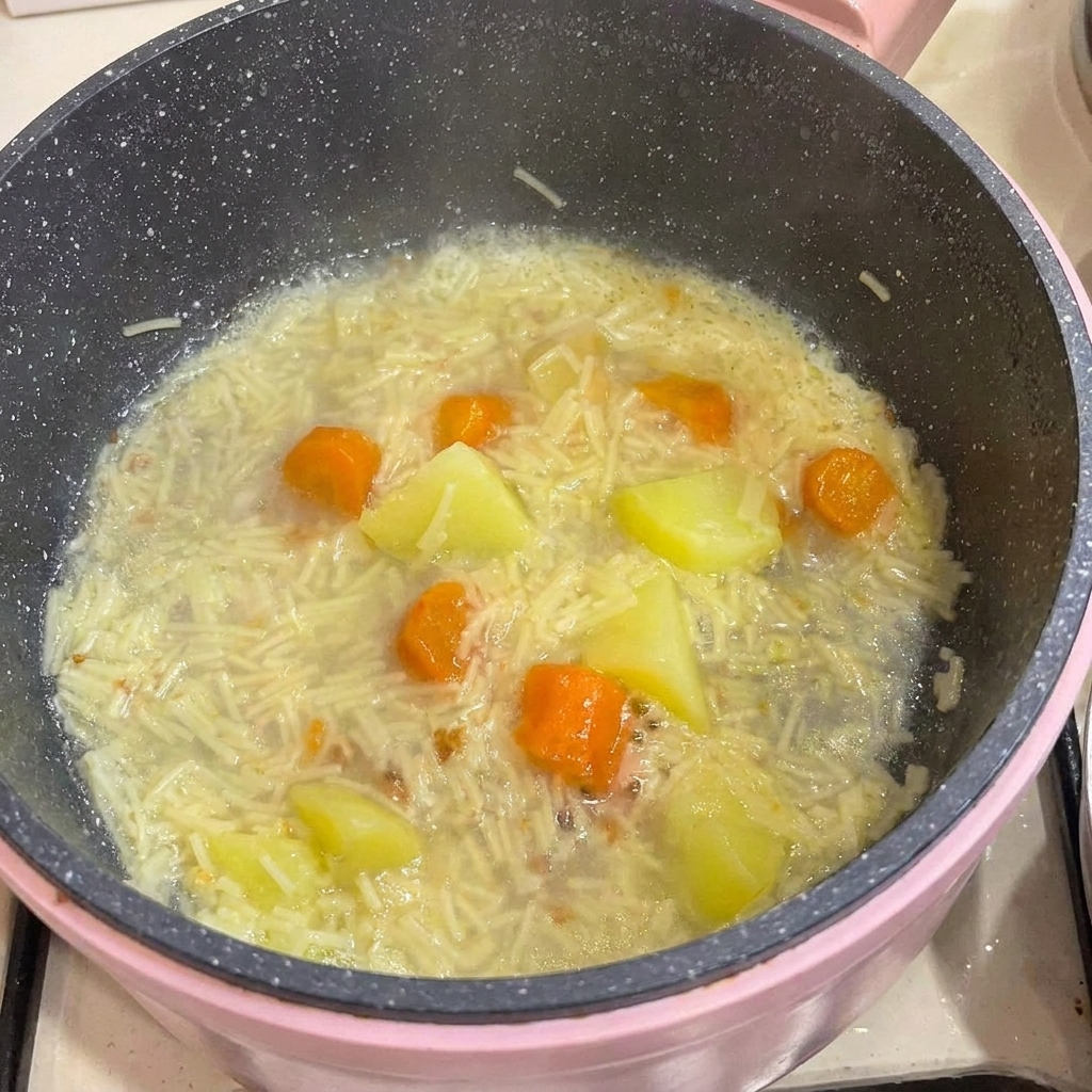 Carne di pollo disossata aggiunta in una pentola piena di pastina cotta, patate e carote nel brodo.