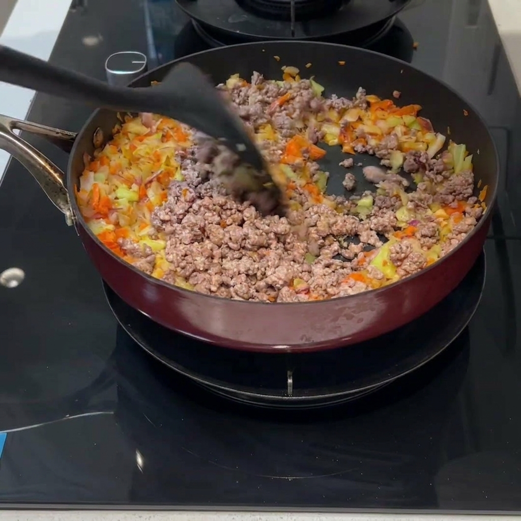 Carne e verdure mescolate insieme in padella con una spatola nera.