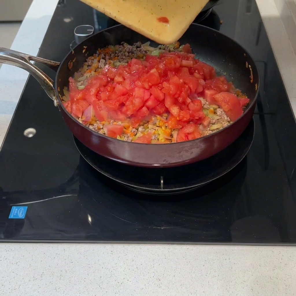 Pomodori freschi a cubetti versati dal tagliere in padella.