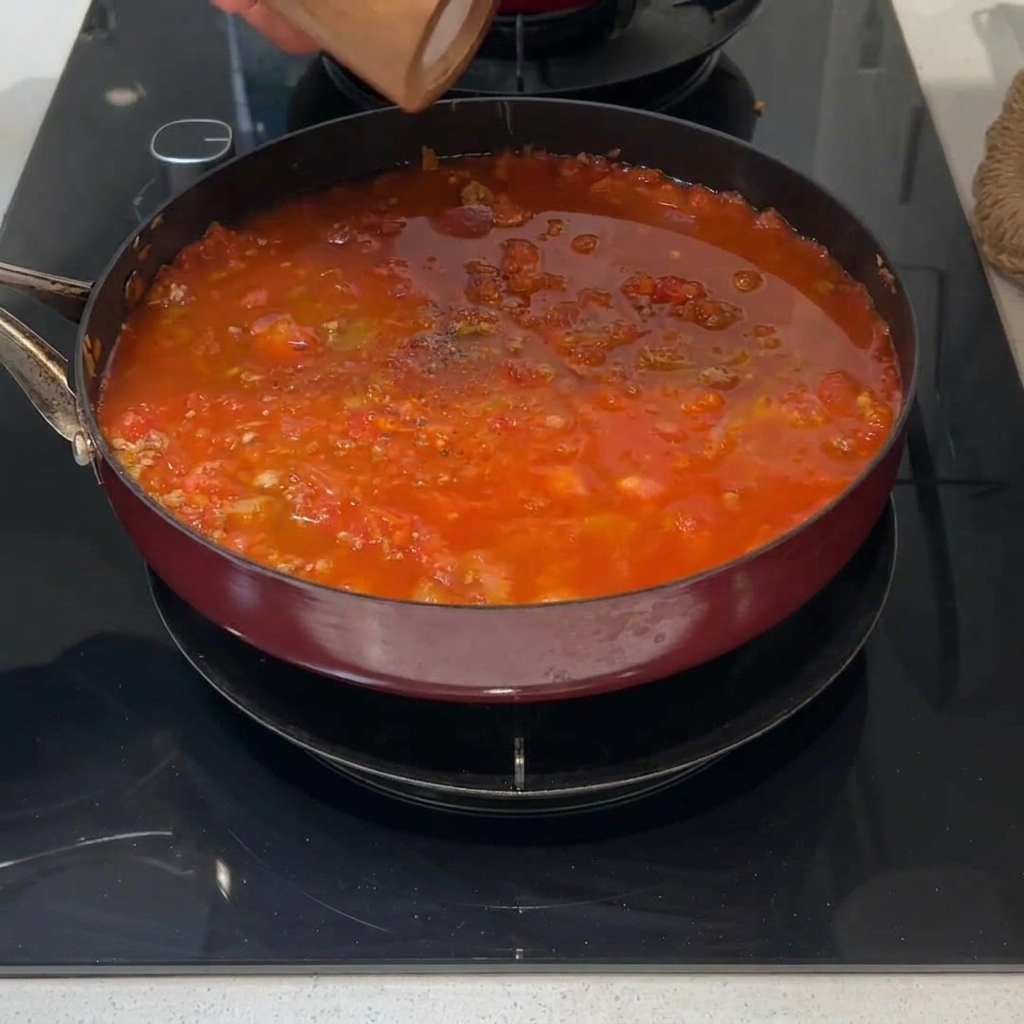Un rametto di rosmarino fresco sopra il sugo di carne in cottura.