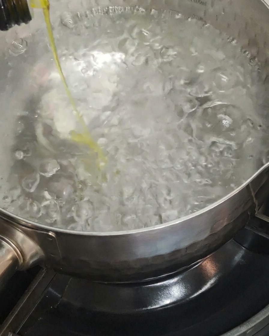 Olio doliva versato in una pentola dacqua bollente.