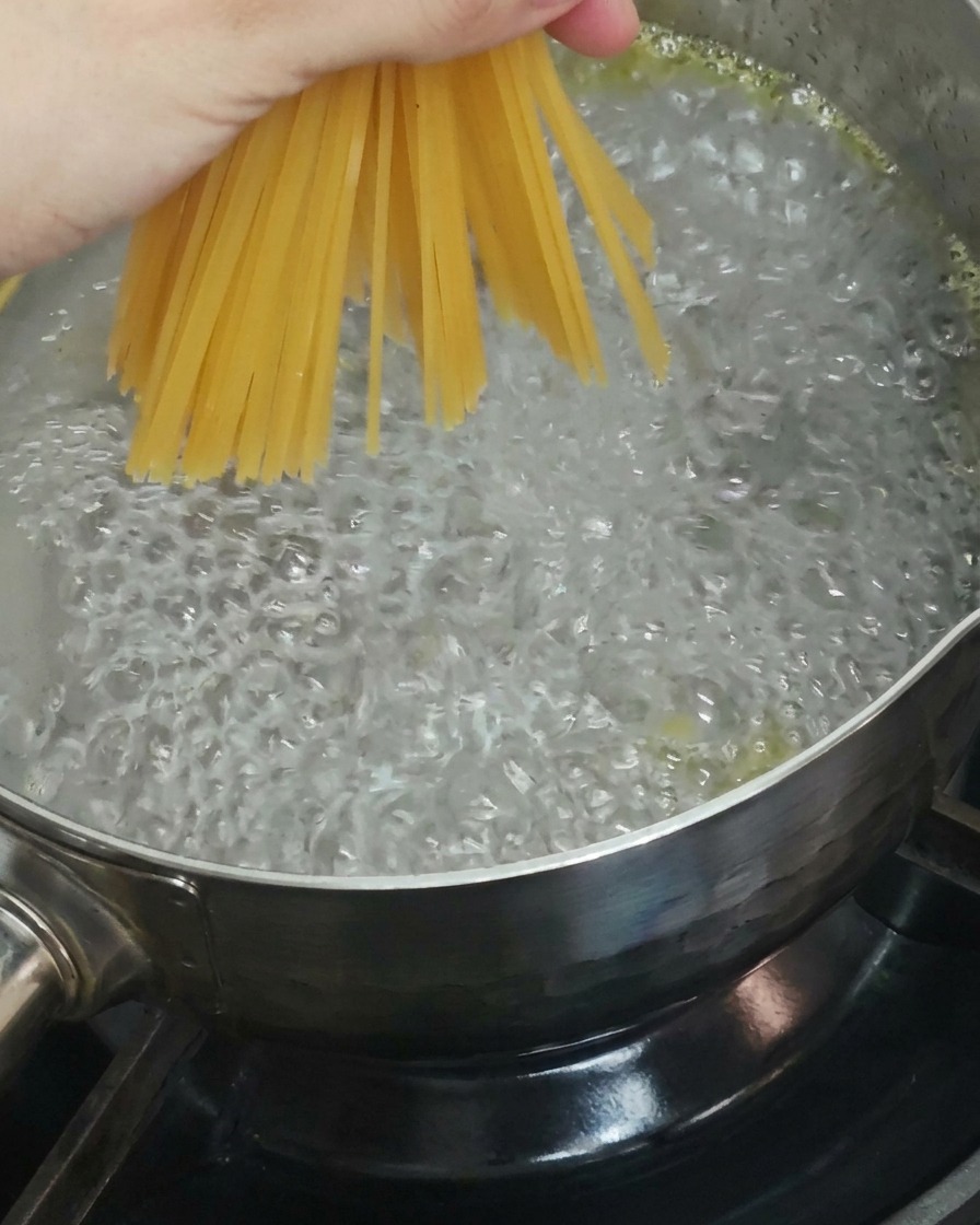 Mano che immerge spaghetti secchi in una pentola dacqua bollente.
