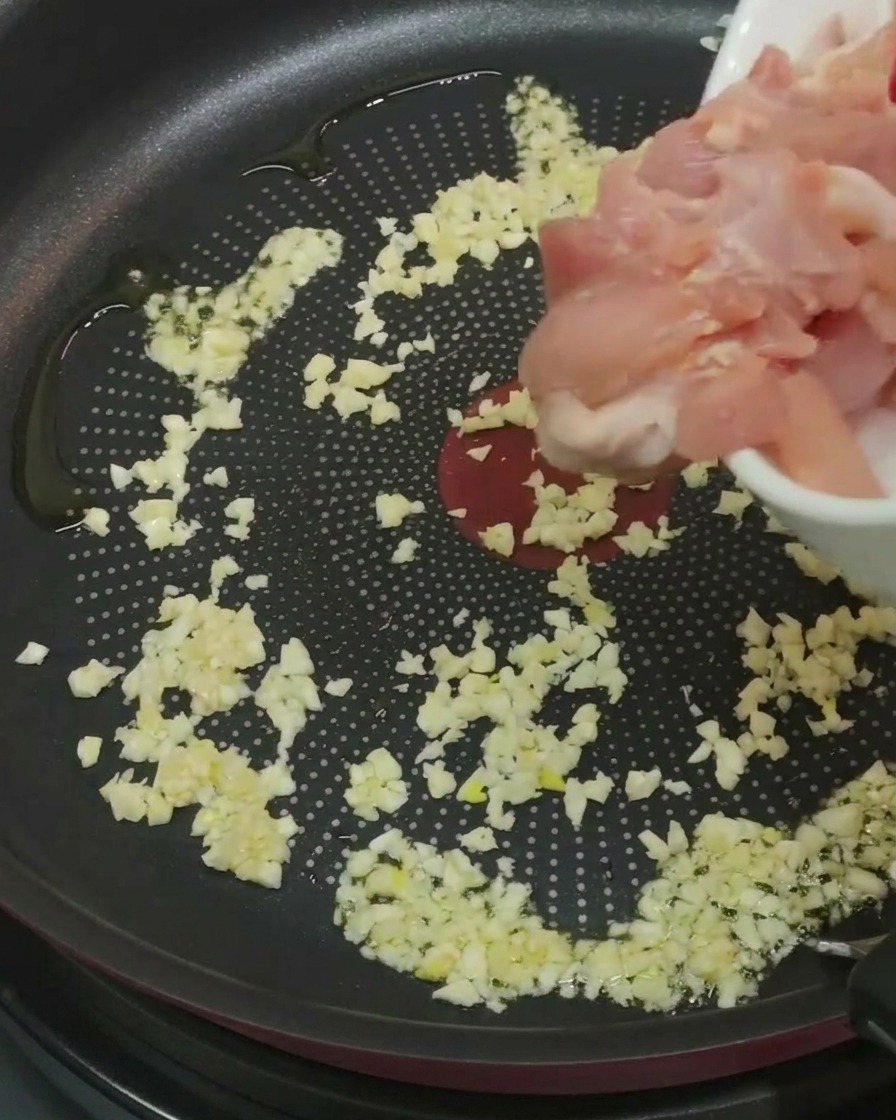 Pezzi di pollo aggiunti nella padella con aglio e olio.