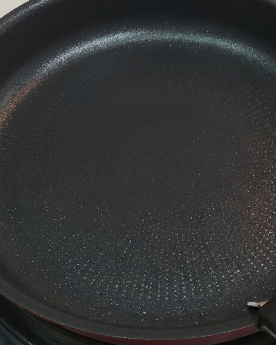 Pinze che girano i pezzi di pollo in padella.