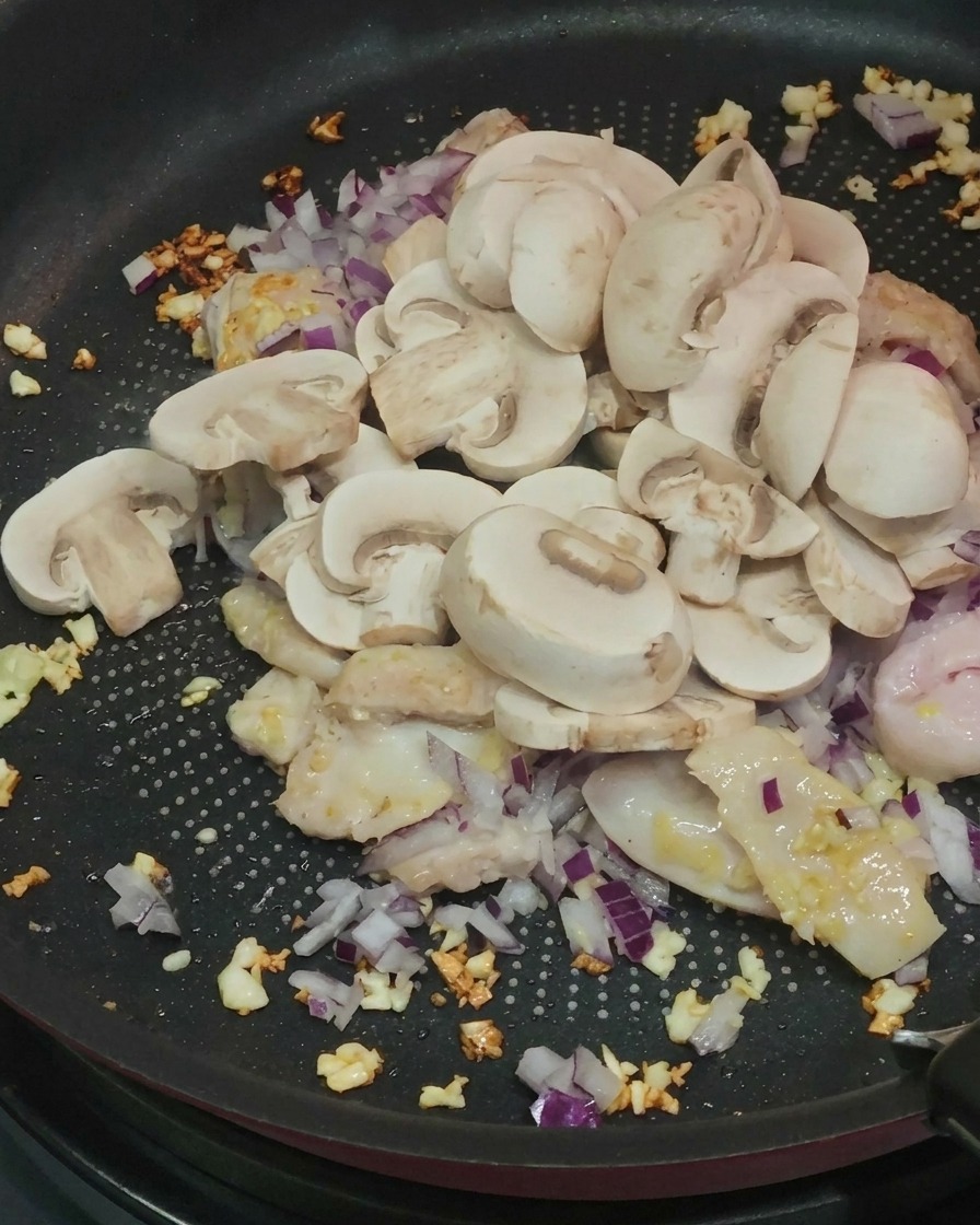 Funghi prataioli affettati aggiunti alla padella con pollo e cipolle.