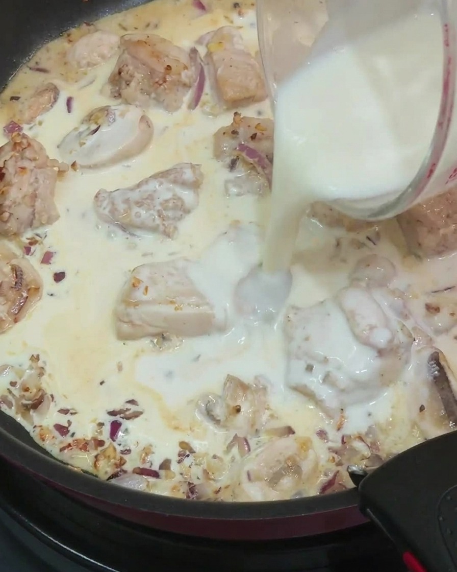 Latte versato da un misurino nella padella con salsa, pollo e funghi.