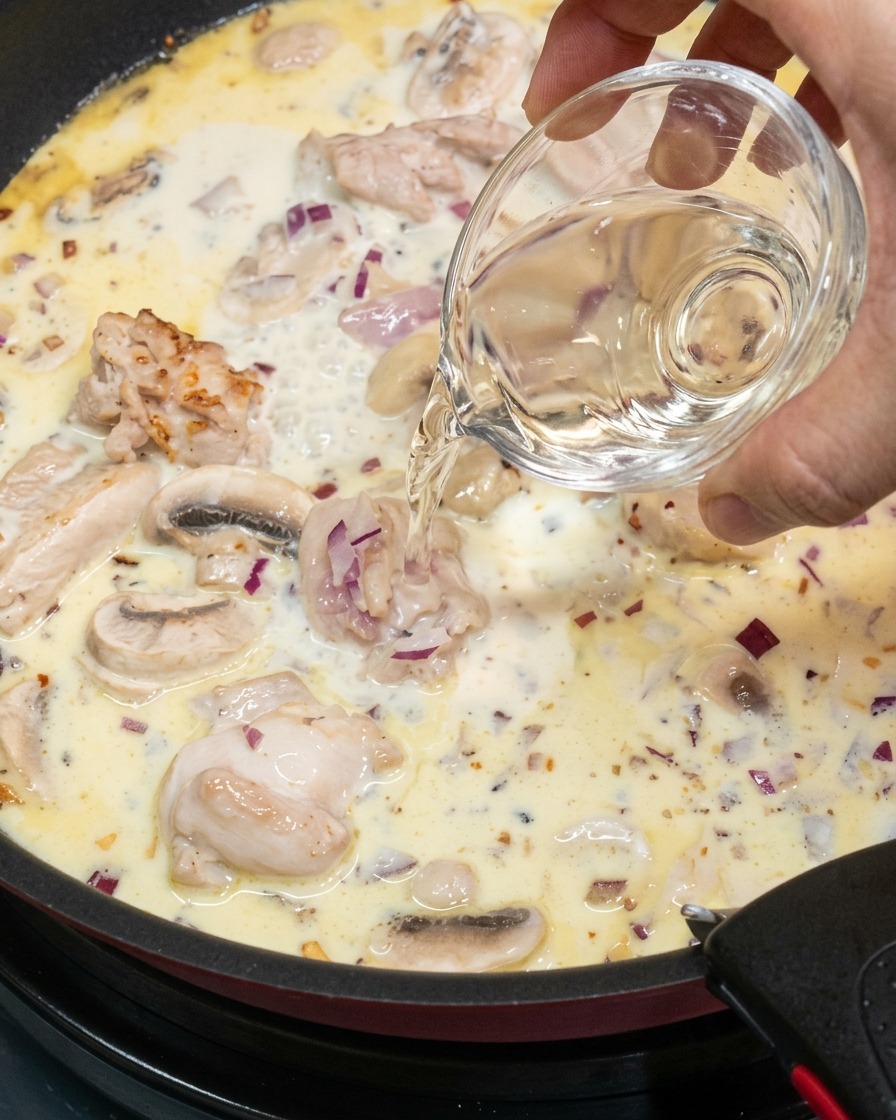 Vino bianco versato in una salsa cremosa che sobbolle.