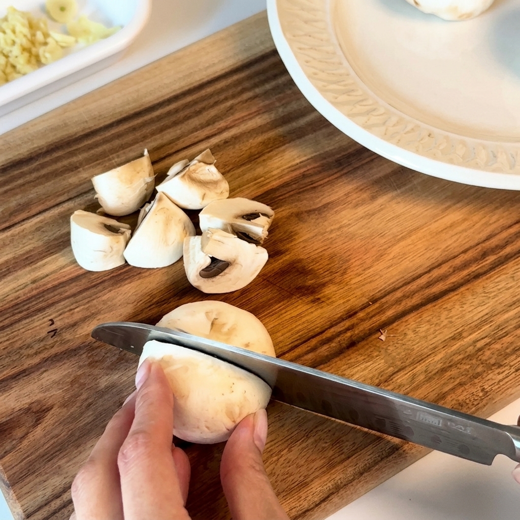 Funghi freschi tagliati a metà o in quarti su un tagliere di legno.