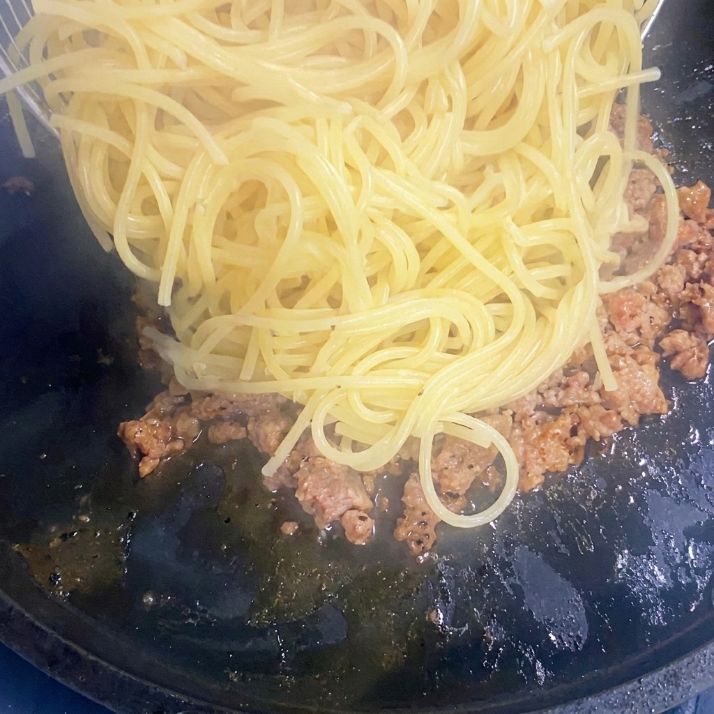 Gli spaghetti cotti vengono aggiunti alla padella con la carne rosolata.