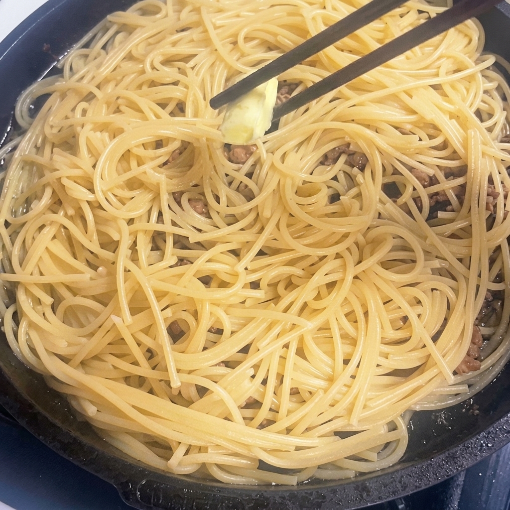 Un tocchetto di burro si scioglie nella padella calda con pasta e carne.