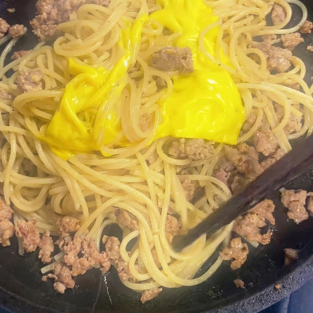 Il formaggio fuso viene mescolato agli spaghetti in padella.