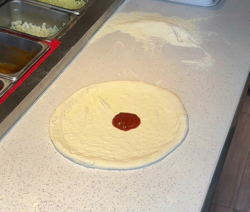 Un cucchiaio di salsa di pomodoro rossa al centro di una base per pizza stesa.