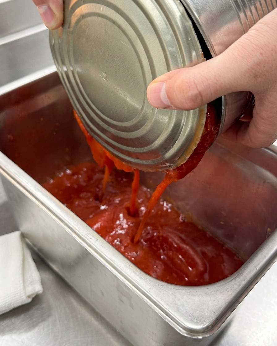 Pomodori pelati versati in un grande contenitore in acciaio inossidabile.