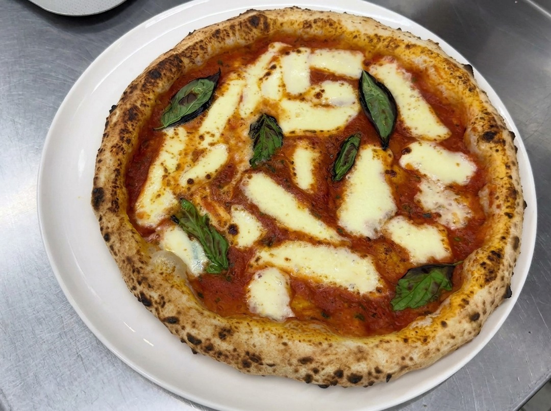 Mani che stendono con cura un panetto di impasto lievitato su un piano di lavoro infarinato, formando un disco perfetto.