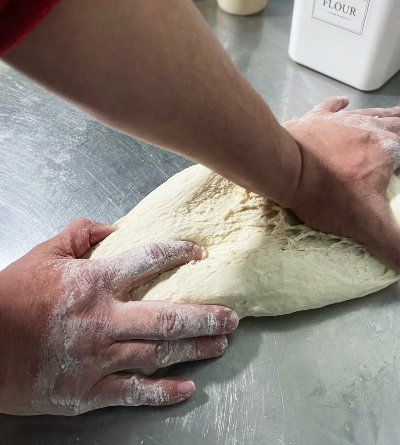 Mani che formano un panetto di pizza liscio.