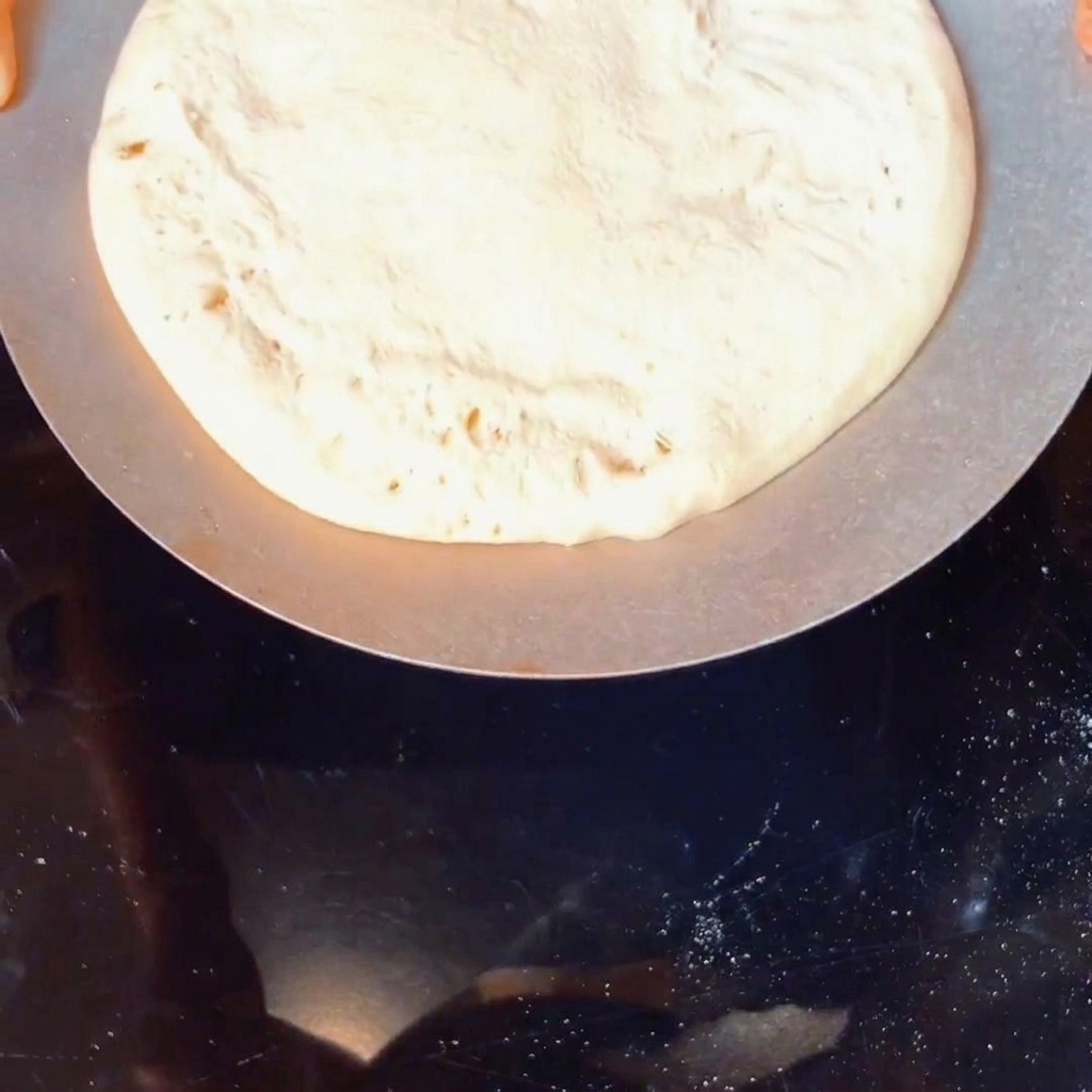 Una pallina di impasto per pizza cruda che viene infarinata con farina di mais in un contenitore.