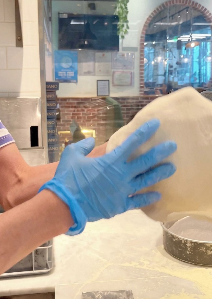 Impasto per pizza lanciato e steso in aria da mani con guanti blu.