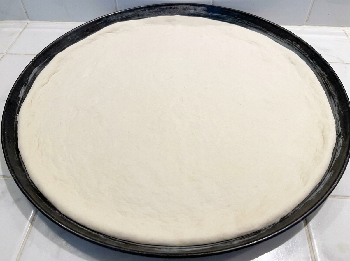 Un disco di impasto crudo per pizza premuto in una teglia rotonda di metallo nero.