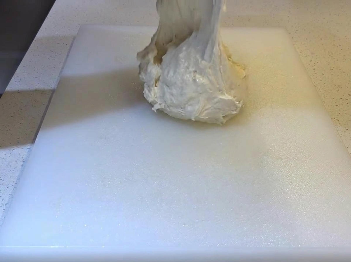 Impasto morbido e appiccicoso che viene fatto cadere su un tagliere bianco oliato.