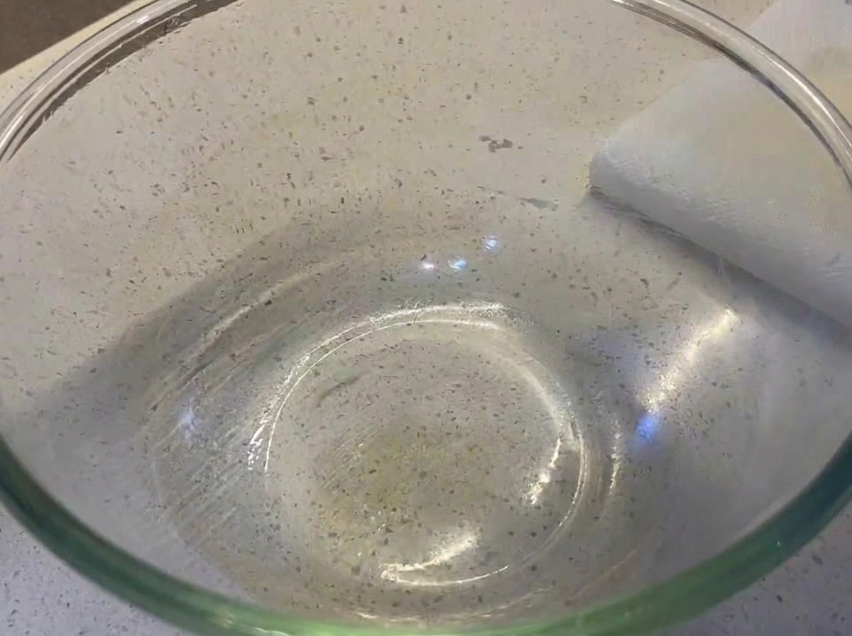 Una palla di impasto liscia e rotonda che riposa allinterno di una ciotola di vetro trasparente leggermente rivestita dolio.