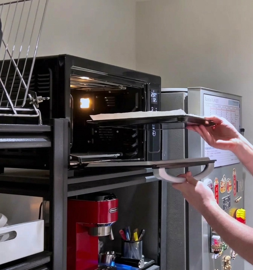 Una persona che rimette una pizza rettangolare carica di formaggio nel forno caldo per la cottura finale.
