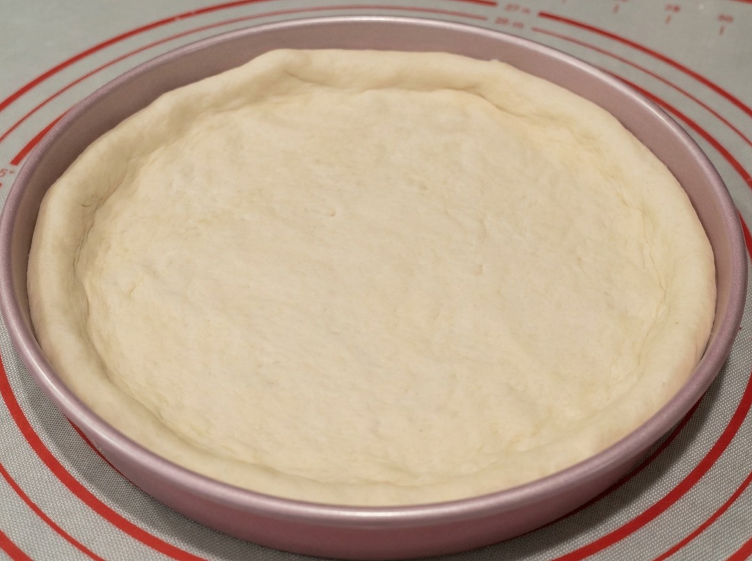 Impasto inserito in una teglia da pizza in metallo da 23 cm con i bordi modellati a mano.