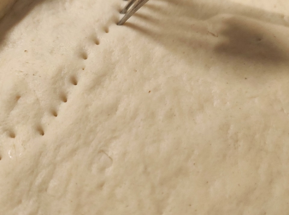 Una forchetta che preme nellimpasto crudo per creare file di fori sulla crosta.