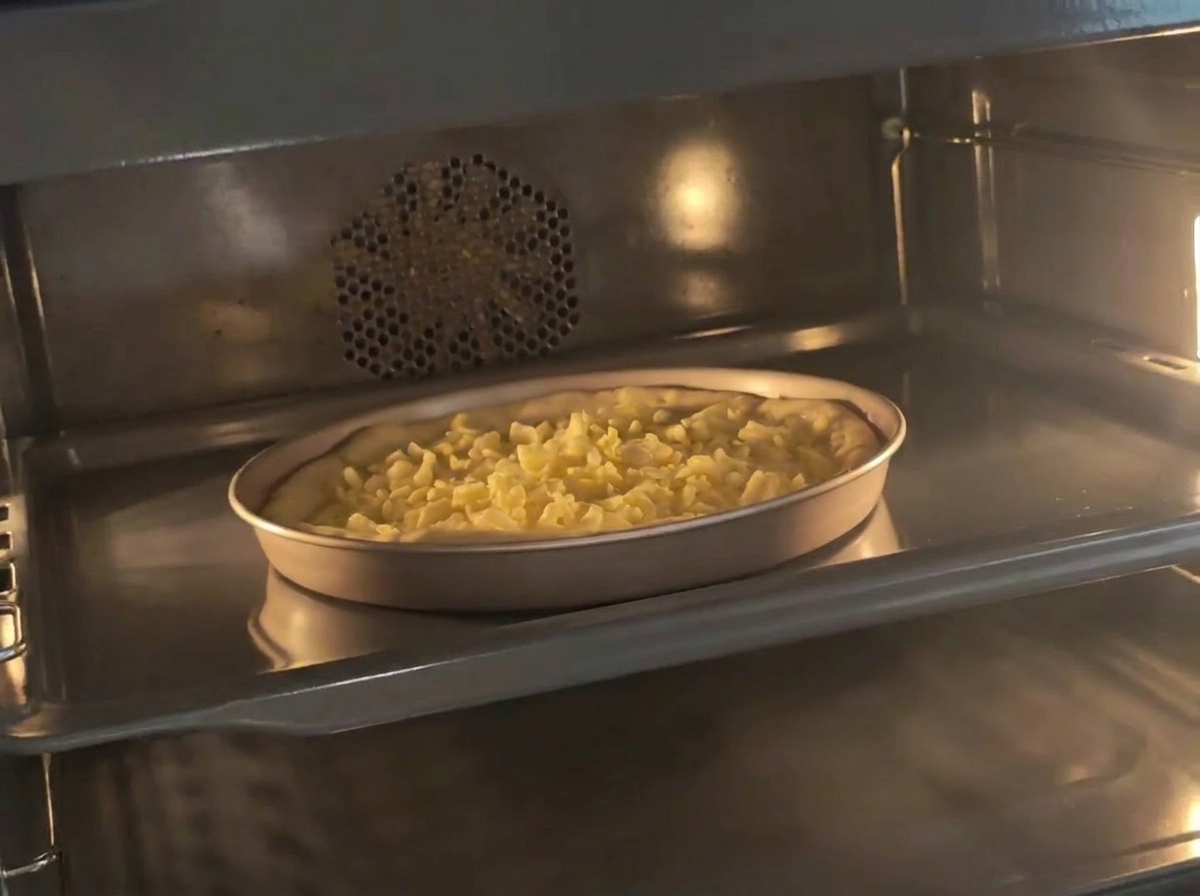 Una teglia contenente limpasto per pizza preparato, ricoperto di formaggio grattugiato, allinterno di un forno preriscaldato.