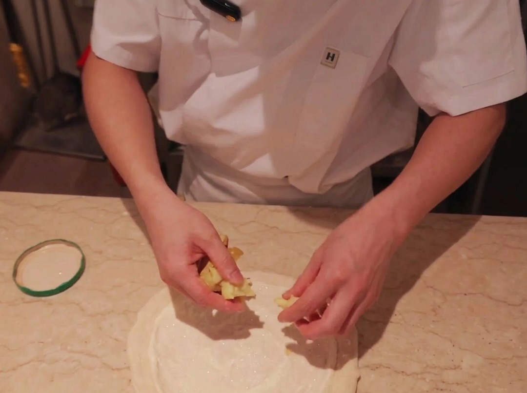 Fette sottili di patata disposte sopra una base di pizza ricoperta di salsa.