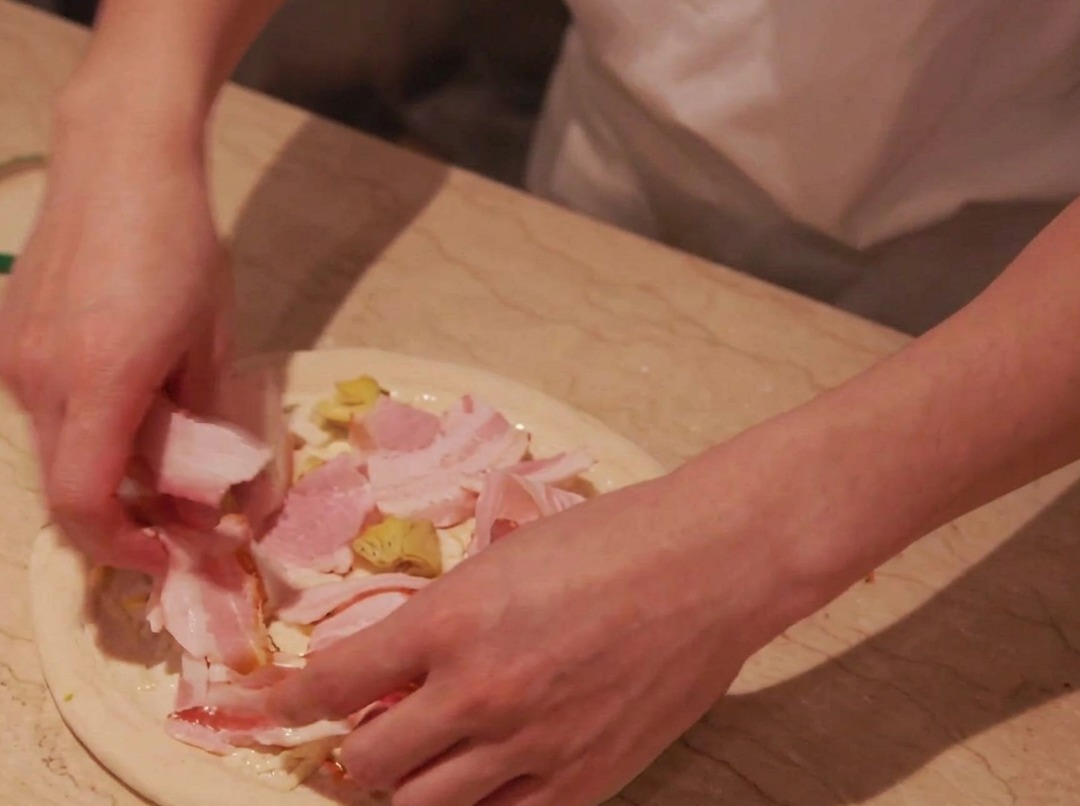 Fette di pancetta disposte con cura sopra lo strato di patate sullimpasto della pizza.