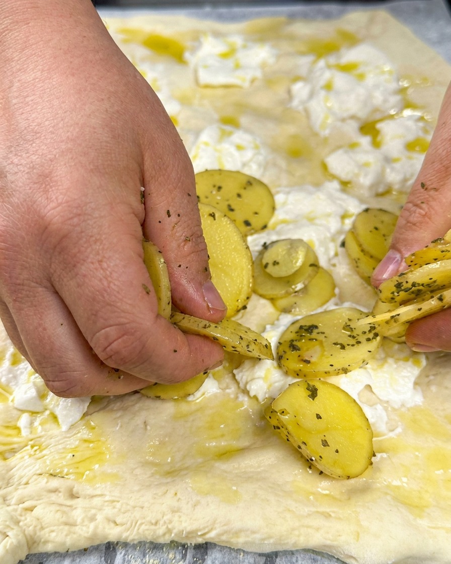 Fettine di patata disposte sulla pizza con erbe fresche.