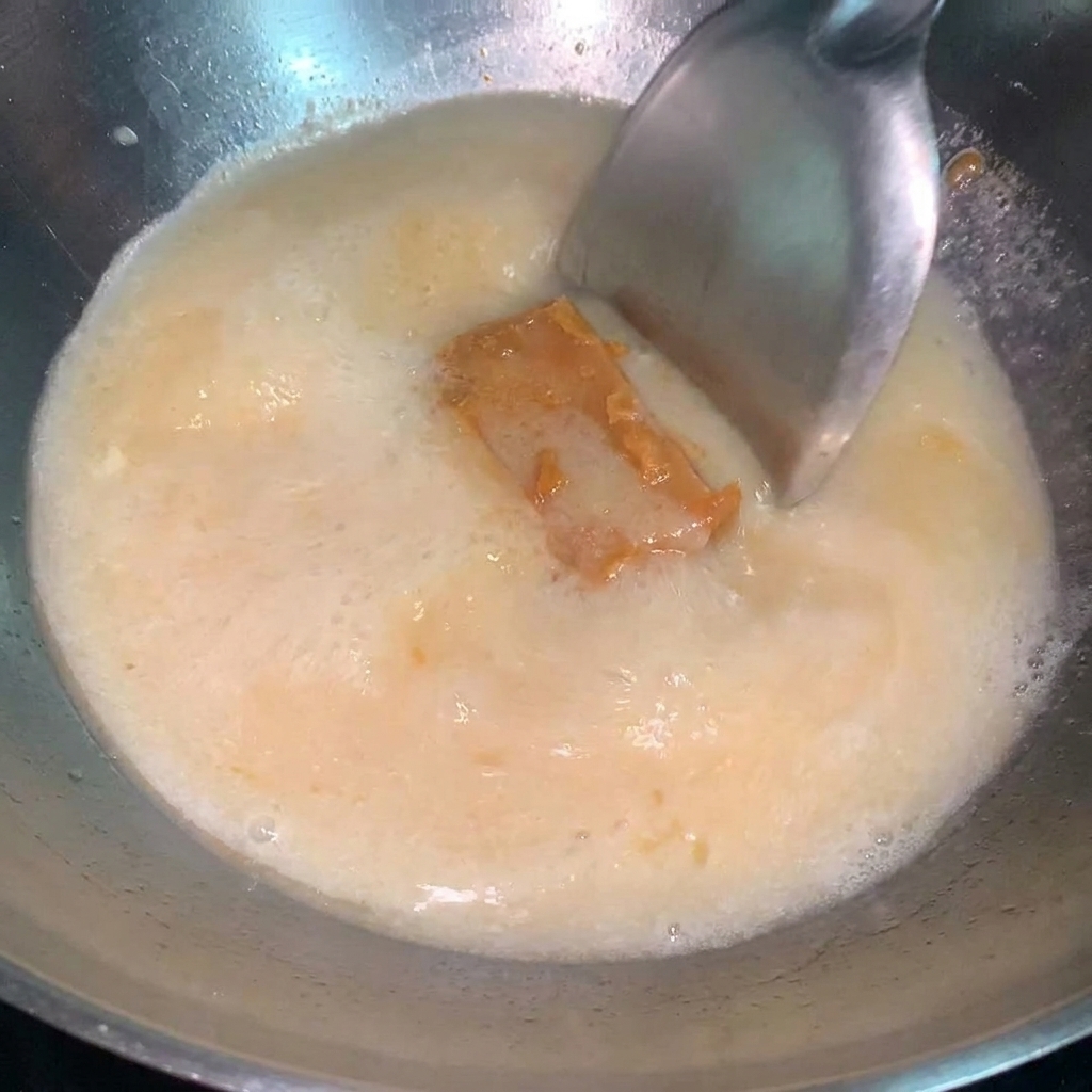 Un cucchiaio di salsa al miso che viene incorporato in una zuppa di ramen in ebollizione.