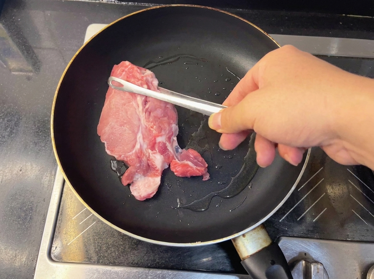 Due pezzi di lonza di maiale cruda che sfrigolano in una padella calda.