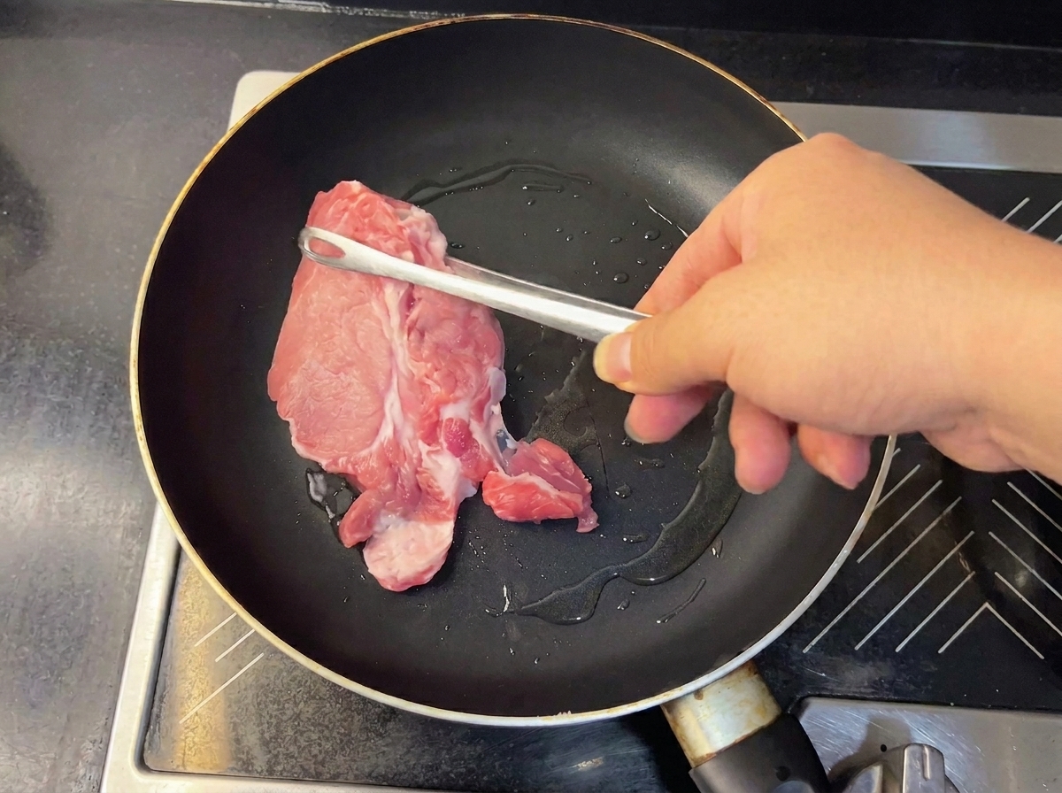 Pezzi di maiale teneri e dorati sollevati dalla padella con pinze metalliche.