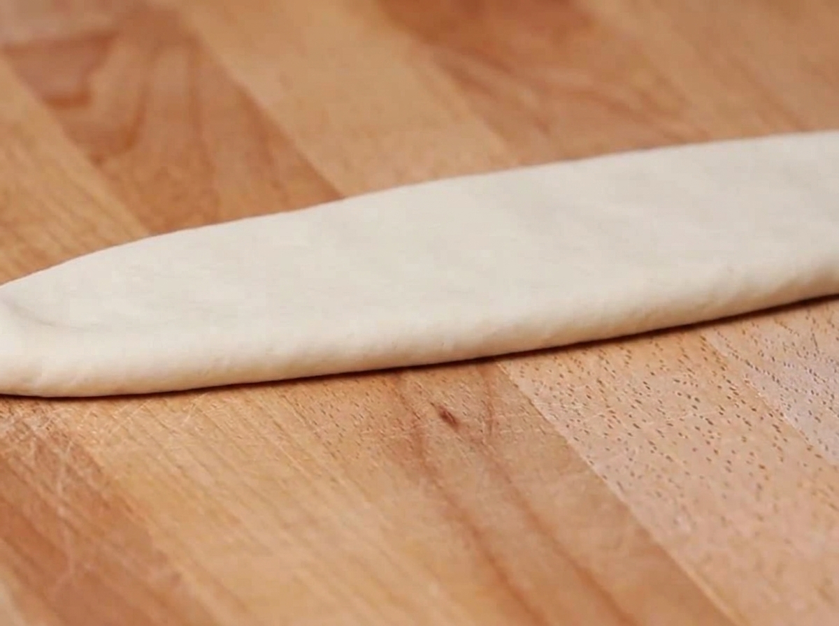 Un foglio di pasta fresca che passa attraverso i rulli di una macchina per pasta.