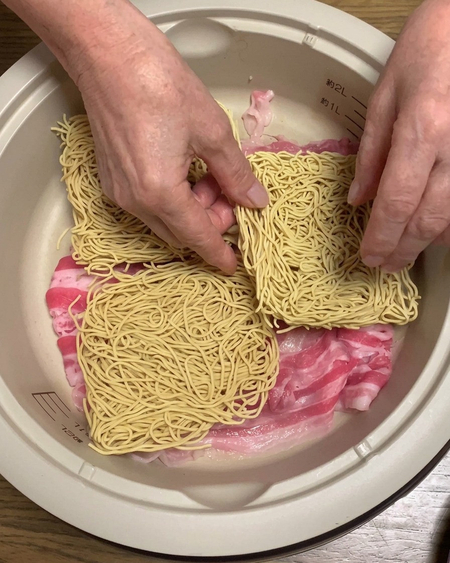 Panetti di noodles secchi per ramen adagiati sopra la pancia di maiale allinterno della pentola.