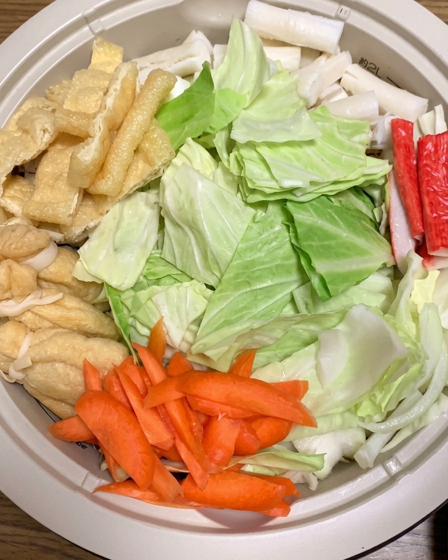 Acqua calda versata in una pentola piena di ingredienti crudi per ramen, inclusi cavolo, carote e tofu fritto.