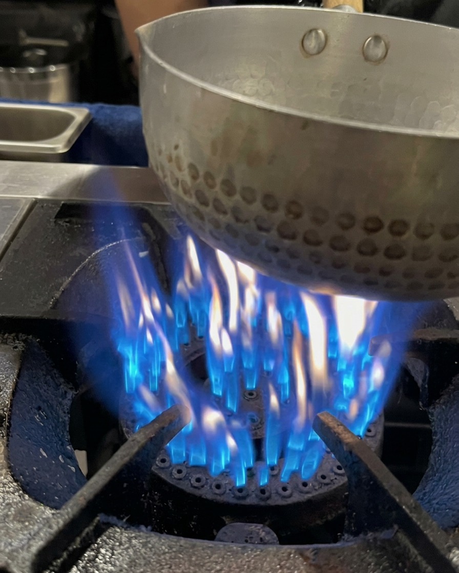 Brodo di ossa di maiale versato in una piccola pentola sopra una fiamma blu a gas attiva.