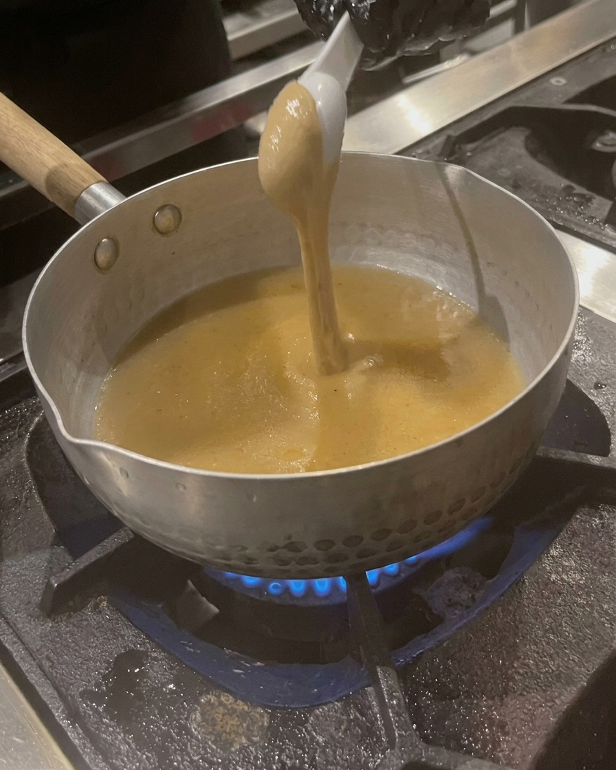 Un cucchiaio di pasta di sesamo densa color marrone chiaro viene mescolato nel brodo in ebollizione nella pentola.