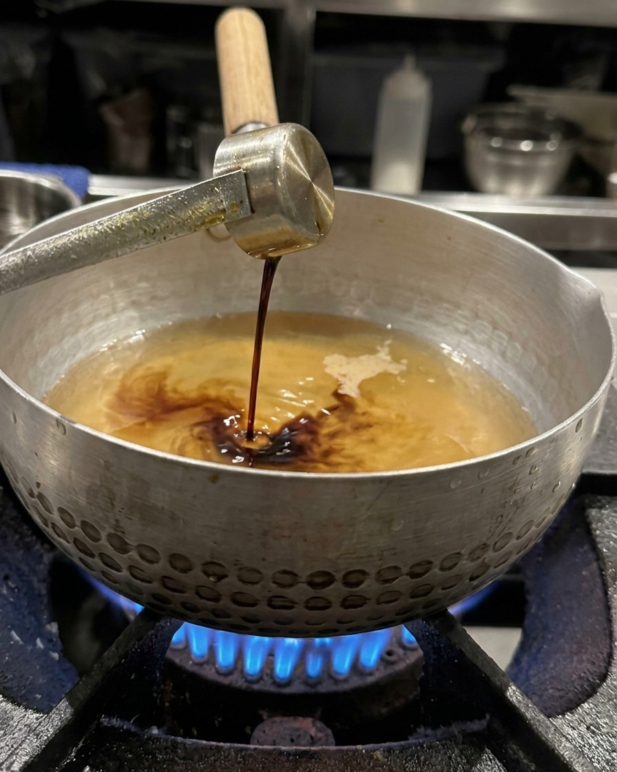 Salsa di soia versata da un mestolo di metallo nel brodo, pronta per essere mescolata.