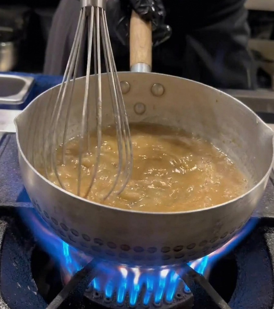 Noodles ramen agitati con una frusta in una pentola di acqua bollente.