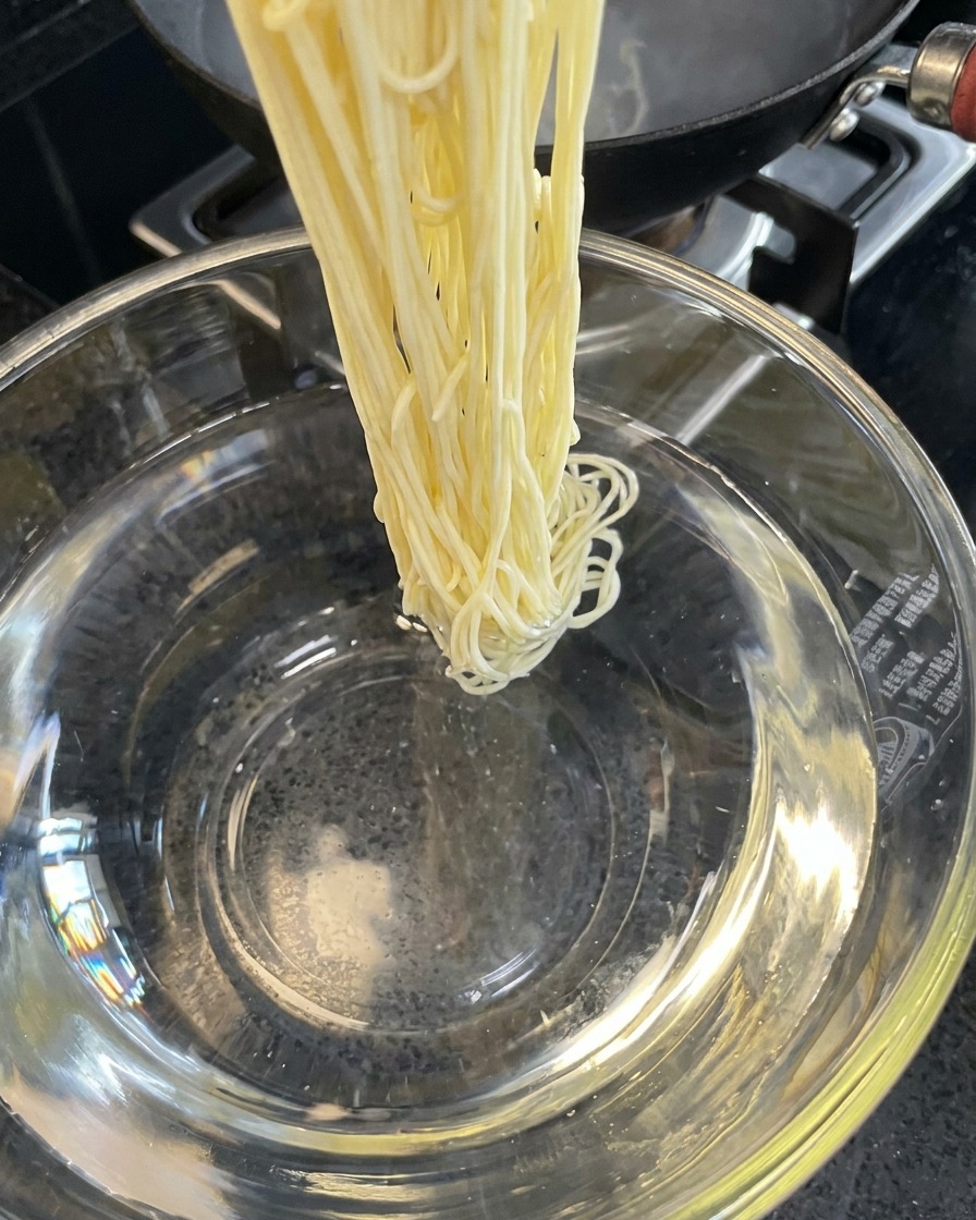 Noodles cotti risciacquati in una ciotola di acqua fredda.