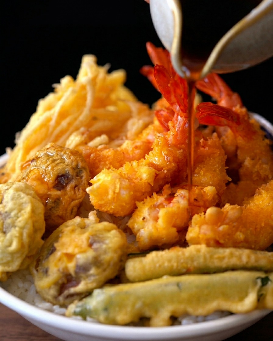 Salsa scura versata da una caraffa su una ciotola di riso e tempura.