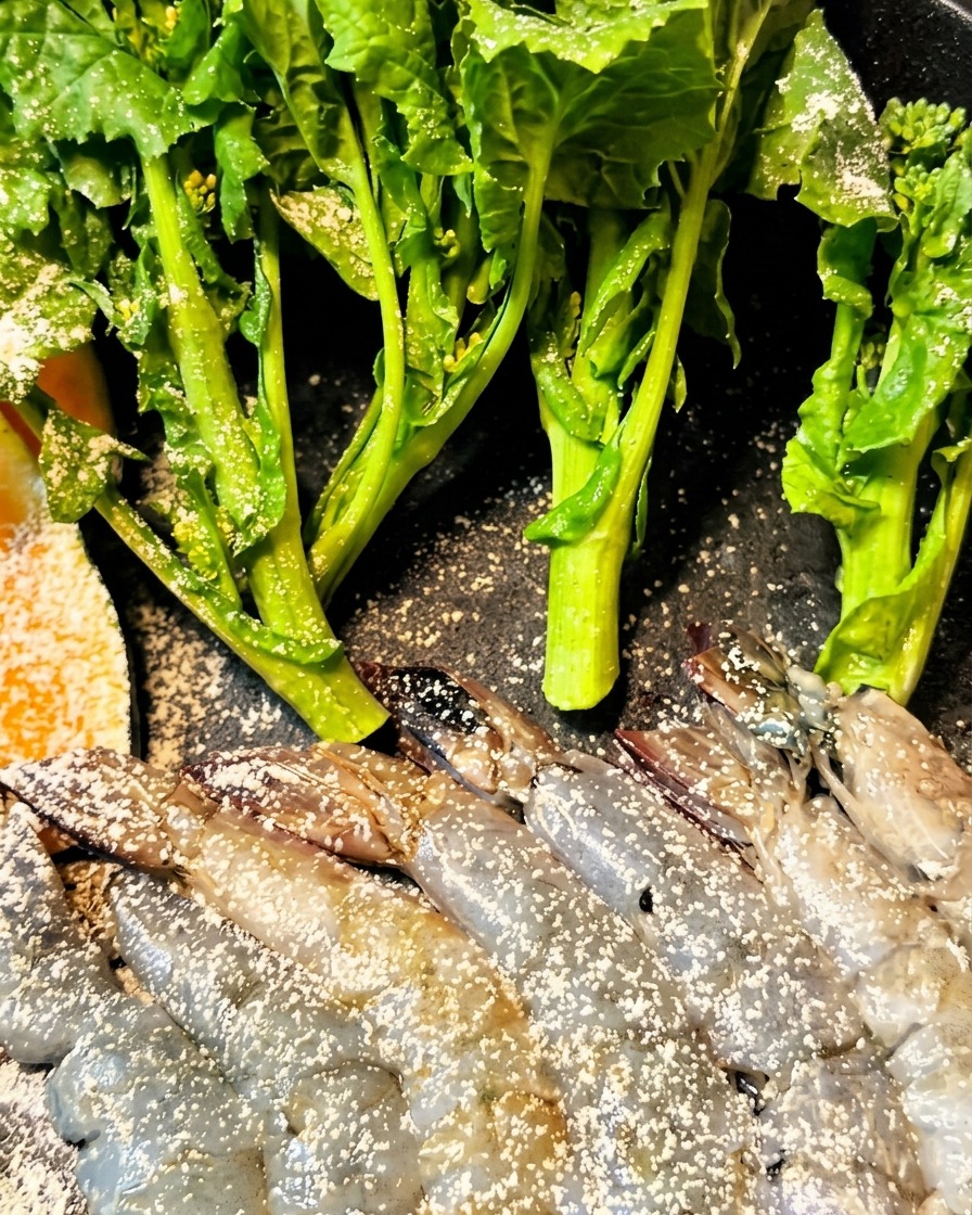 Gamberi e melanzane rivestiti di pastella e inseriti in una friggitrice.
