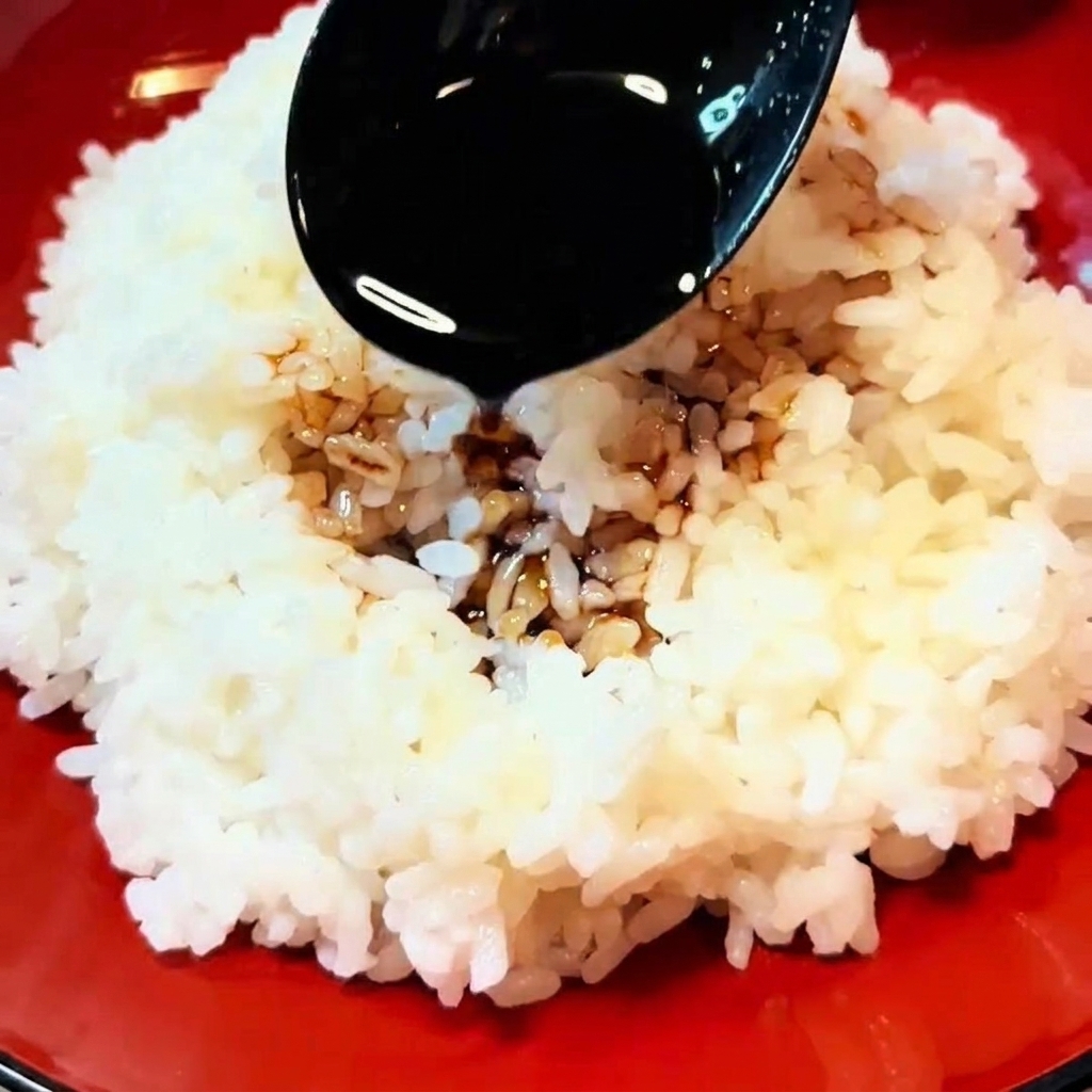 Un cucchiaio nero versa la salsa scura su una ciotola di riso bianco fumante.
