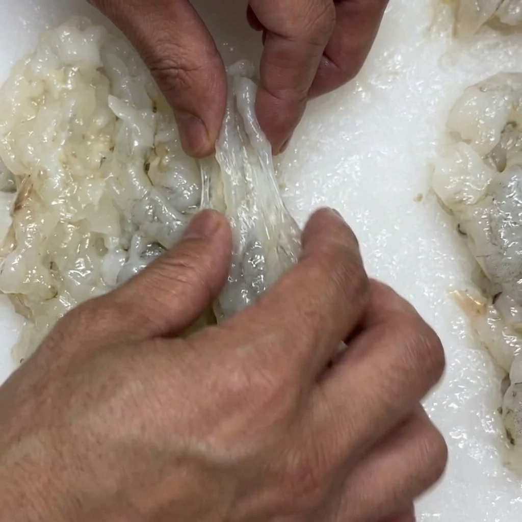 Mani che premono delicatamente un gambero preparato per allungarlo prima di pastellarlo.