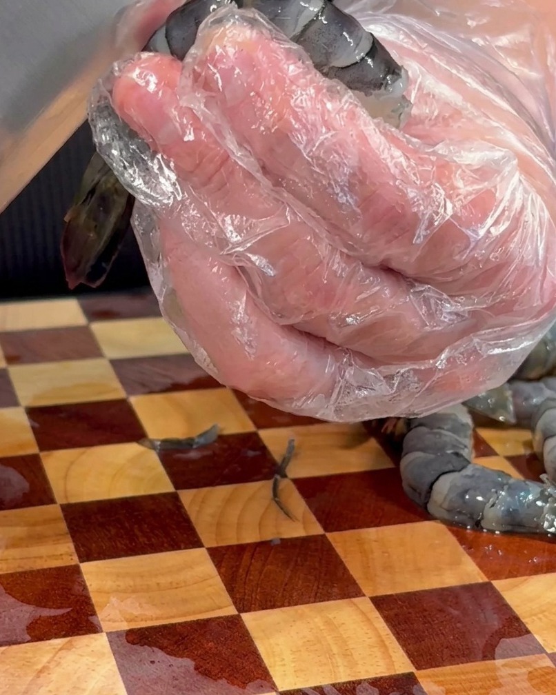 Primo piano di una punta di coltello che rimuove il filo scuro dal dorso di un gambero crudo.